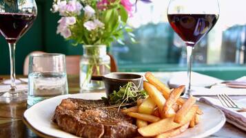 A plate with steak and fries, a glass of red wine, and a vase with flowers on a table.
