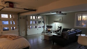A spacious room with a bed, a sofa, a coffee table, and a desk. There are multiple windows and a door leading to an outdoor area.