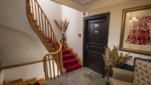 A staircase with red carpet, a black door with a number plate, a framed artwork, and a leather sofa. - Mezzo Hotel (Istanbul)