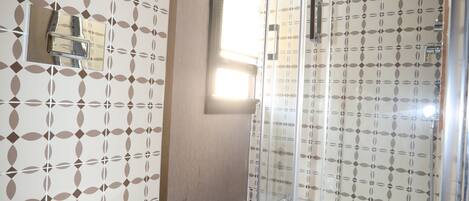 A bathroom with a toilet, a shower with a glass door, and patterned tiles.