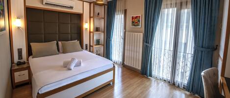 A hotel room with a large bed, bedside tables, an air conditioning unit, a wardrobe, and a window with curtains.