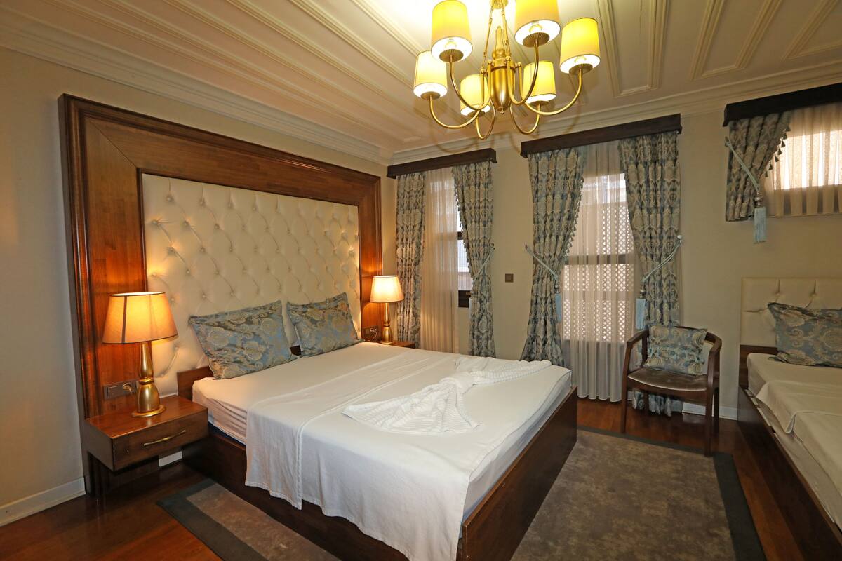 A spacious bedroom with a large bed, two bedside tables with lamps, a chandelier, and a chair.