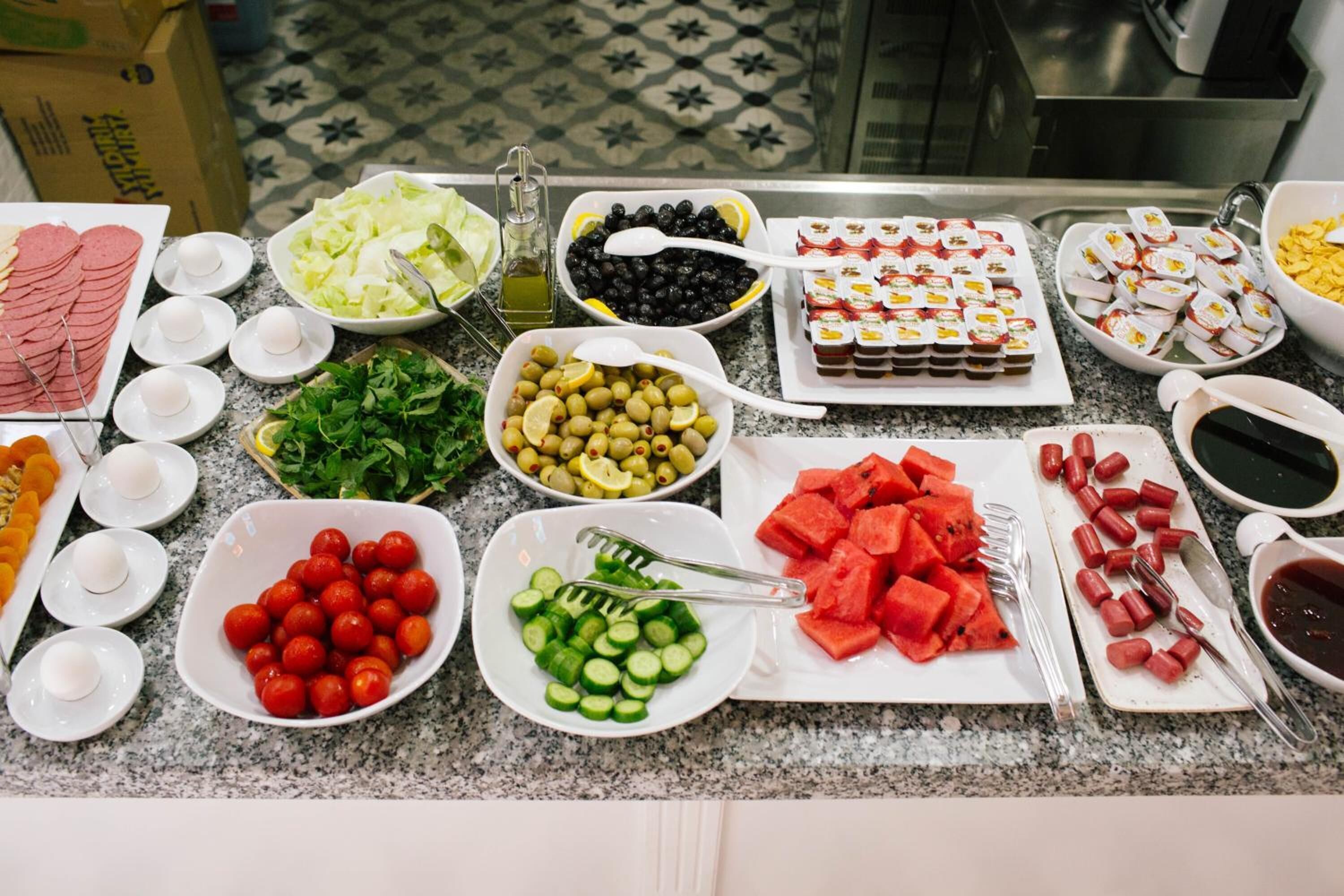A buffet table with various food items including sliced meats, olives, cucumbers, tomatoes, and watermelon.