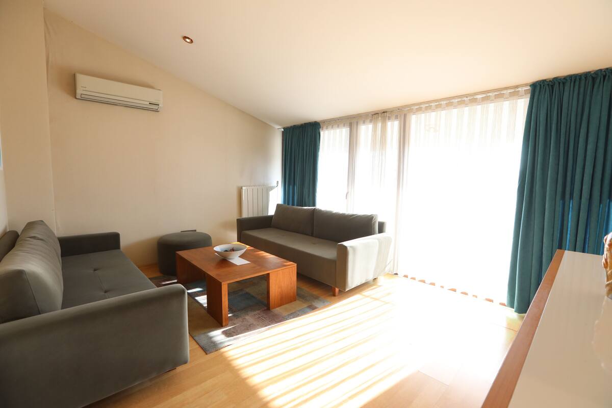 A modern living room with a sofa, a coffee table, and a window with curtains.