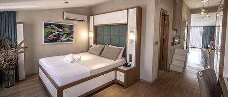A modern hotel room with a large bed, bedside tables, a wall-mounted air conditioner, and a painting.
