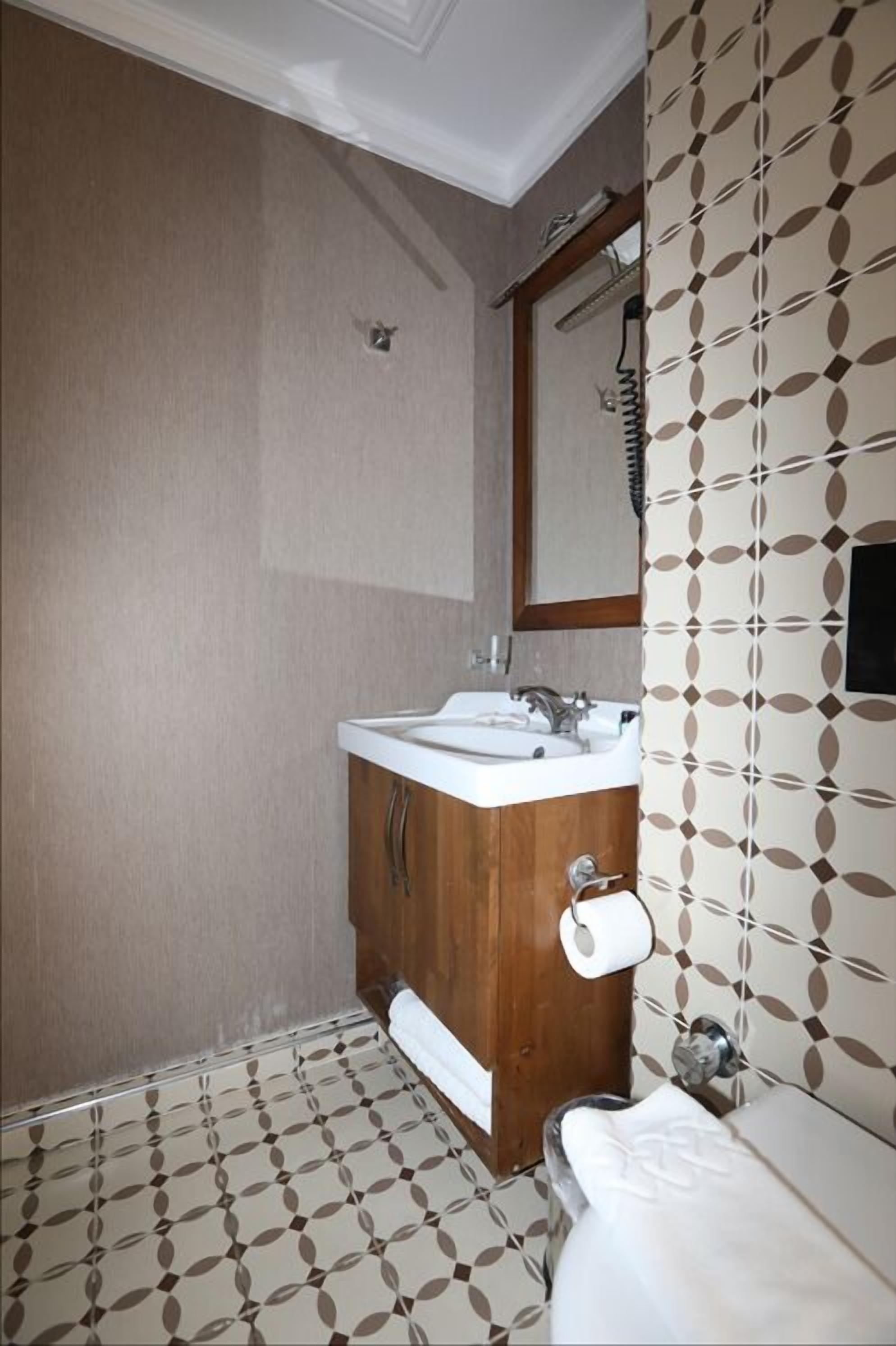 A bathroom with a wooden vanity, a sink, a mirror, and patterned wallpaper.