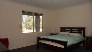 A bedroom with a bed, a nightstand, a window, and a red chair.