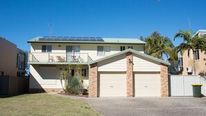 Una casa de dos pisos con garaje, paneles solares y un pequeño jardín delantero con una palmera.