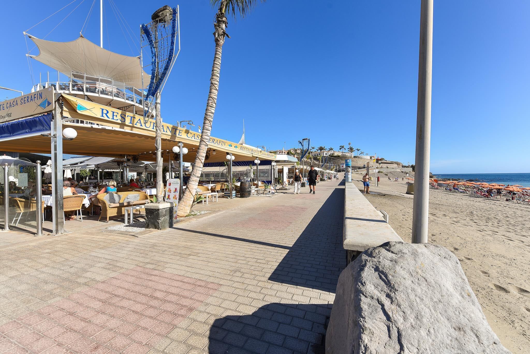Un restaurant en bord de mer avec une terrasse, un palmier et une vue sur la plage.