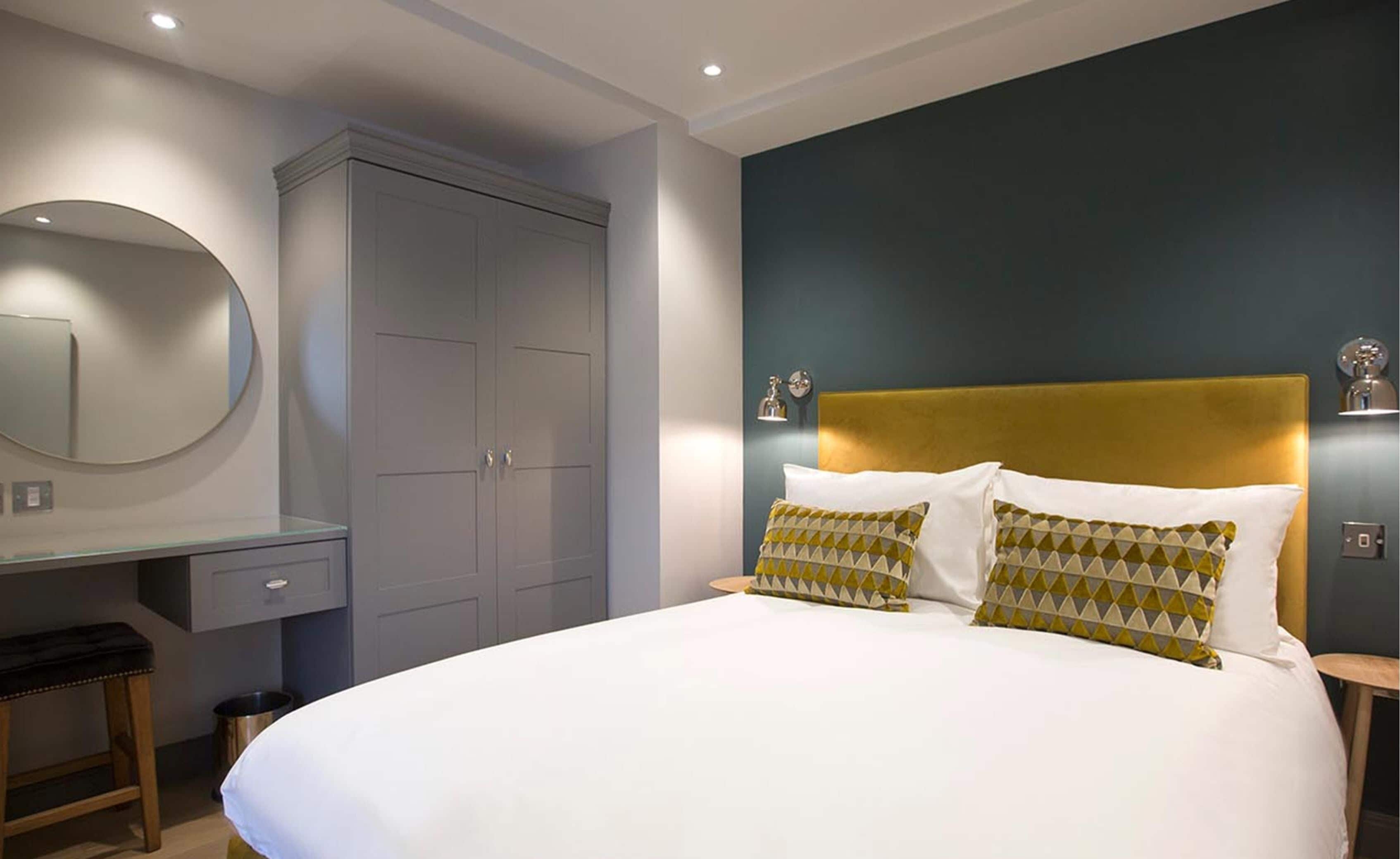A bedroom with a bed, a desk, a wardrobe, and a mirror.