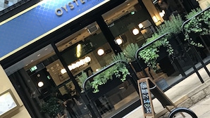 The exterior of the Oyster Club, featuring a blue facade, large windows, and outdoor seating with greenery. - No.8 Waterloo Apartments (Birmingham)