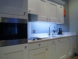 Una cucina moderna con mobili bianchi, un forno a microonde in acciaio inossidabile, un lavello con rubinetto e una macchina da caffè.