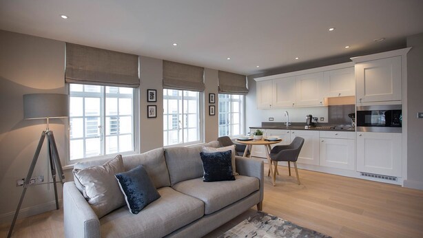 A modern living room with a sofa, a coffee table, and a lamp. There is a kitchen area with cabinets and a dining table. - No.8 Waterloo Apartments (Birmingham)