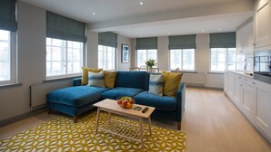 A modern living room with a blue sofa, a wooden coffee table with fruit, and a geometric patterned rug. - No.8 Waterloo Apartments (Birmingham)