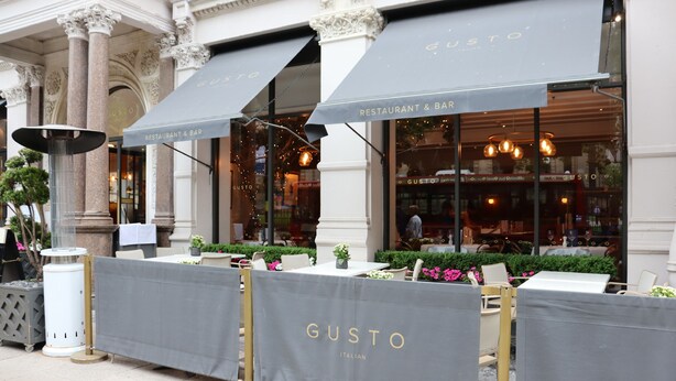 An outdoor seating area with tables and chairs, covered by a grey awning with 'GUSTO ITALIAN' written on it. - No.8 Waterloo Apartments (Birmingham)