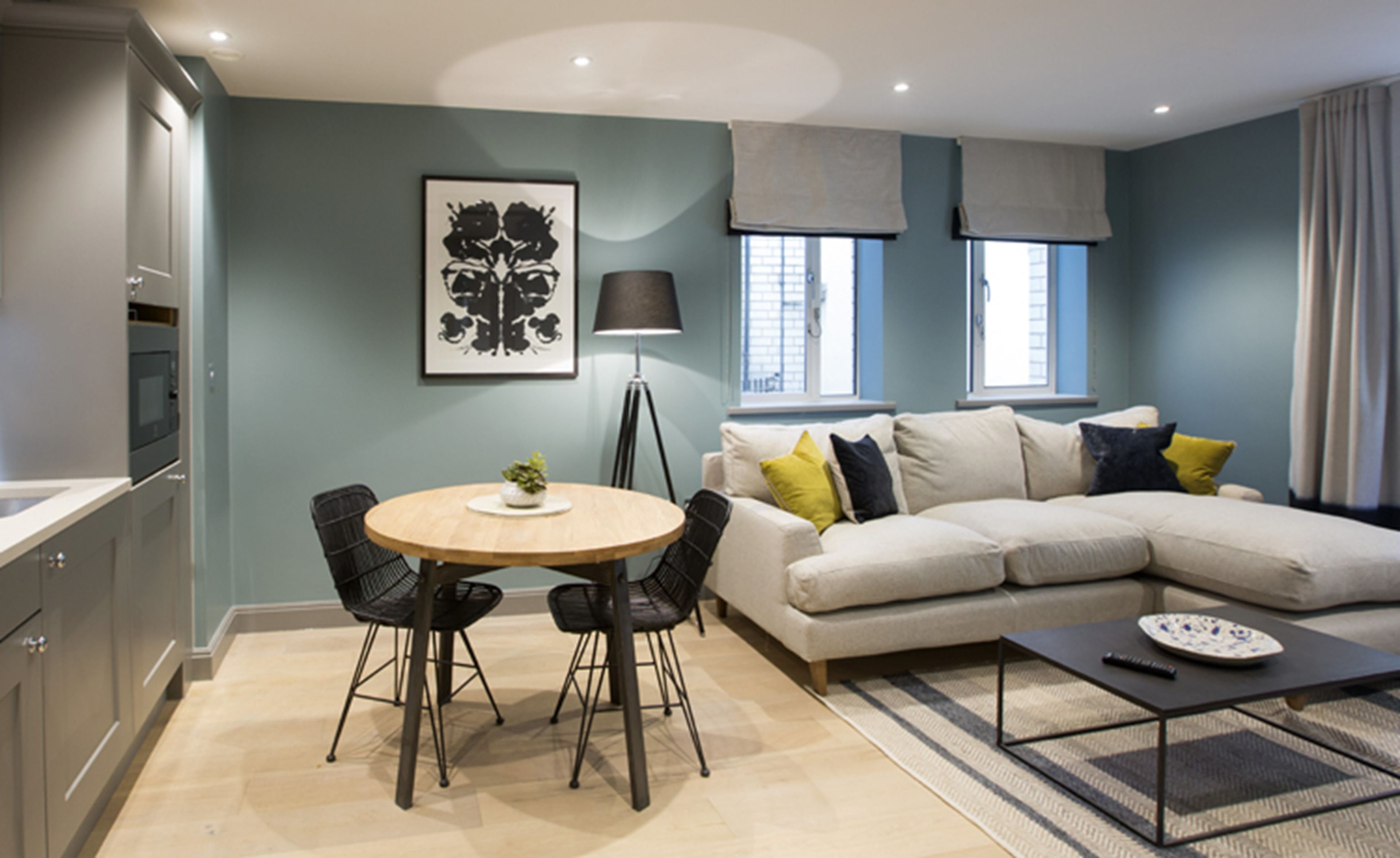 A modern living room with a beige sectional sofa, a round dining table with four chairs, a floor lamp, and a coffee table.