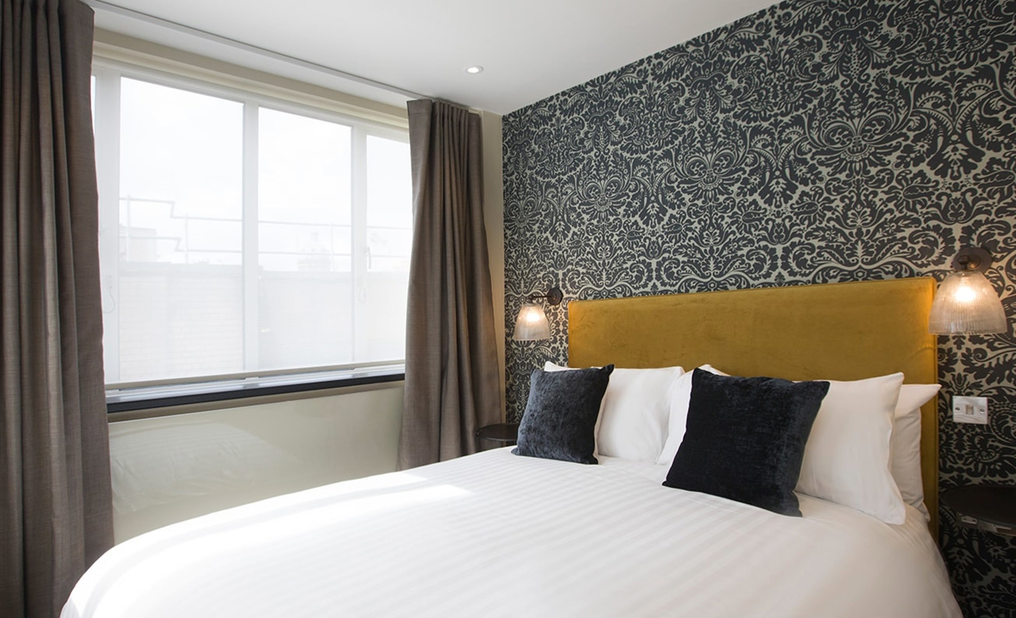 Une chambre d’hôtel avec un grand lit, un papier peint à motifs et une vue par la fenêtre.