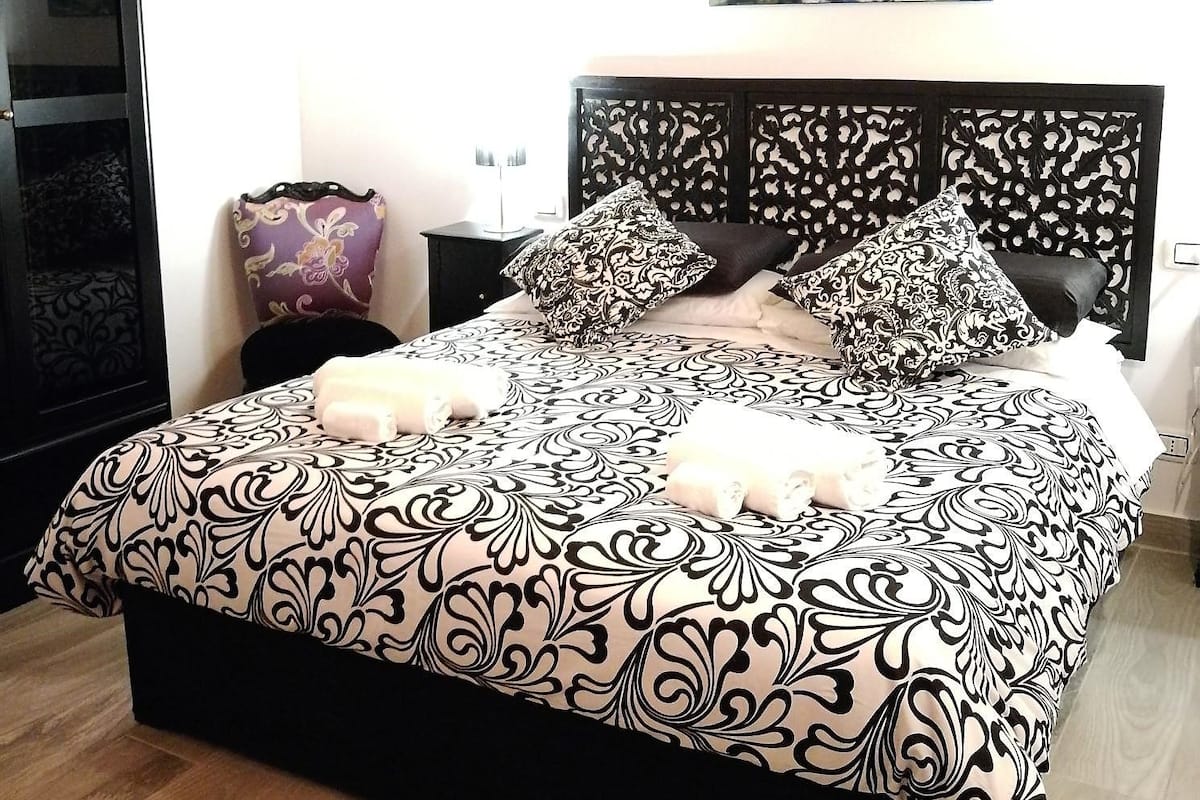 A bedroom with a large bed, a nightstand, a lamp, and a painting on the wall.