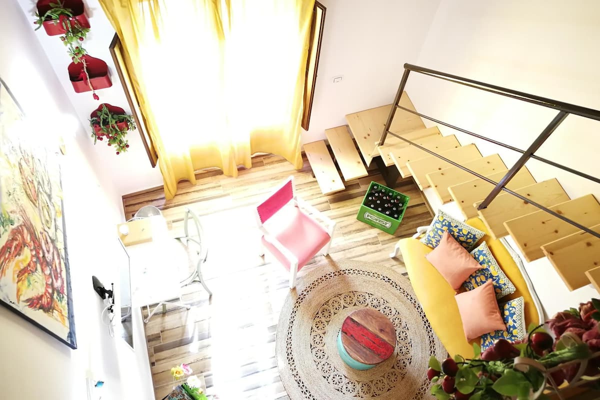 A bright room with a staircase, a dining table, and a large window with yellow curtains.