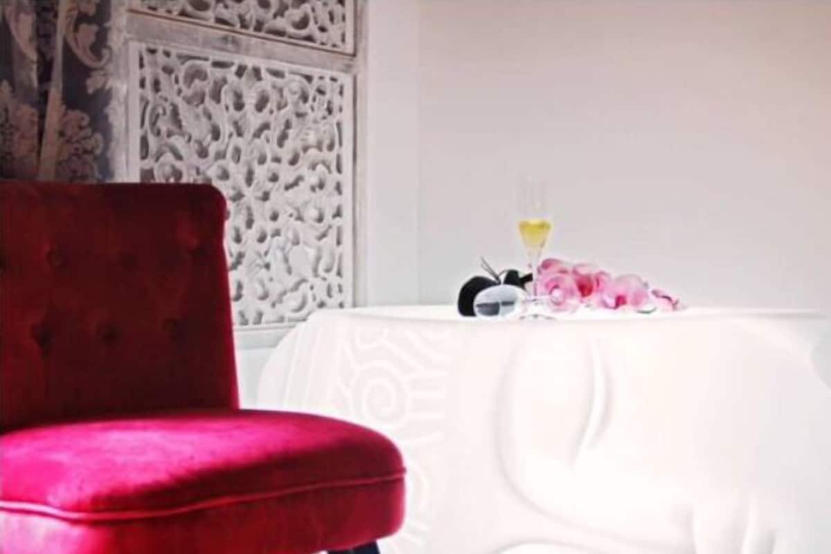 A red velvet chair and a white table with a glass and flowers.