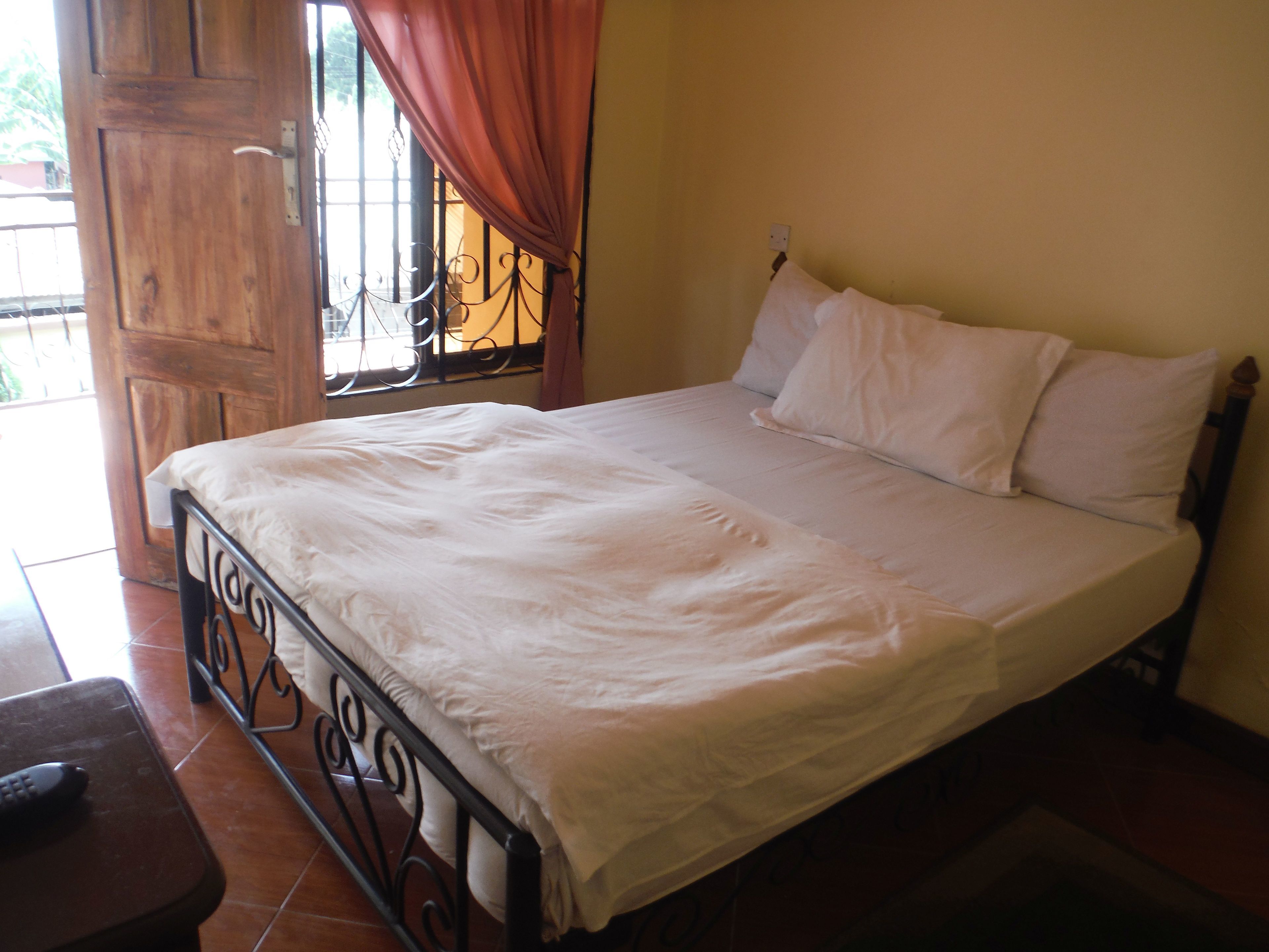 A bedroom with a bed, a wooden door, and a window with curtains.