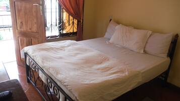 A bedroom with a bed, a wooden door, and a window with curtains.