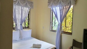 A bedroom with a bed, white curtains, and a window with a metal grill. - Bright Star Hotel (Arusha)