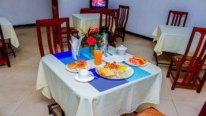 A dining area with tables set for breakfast, including bread, fruit, and a hot beverage. - Bright Star Hotel (Arusha)