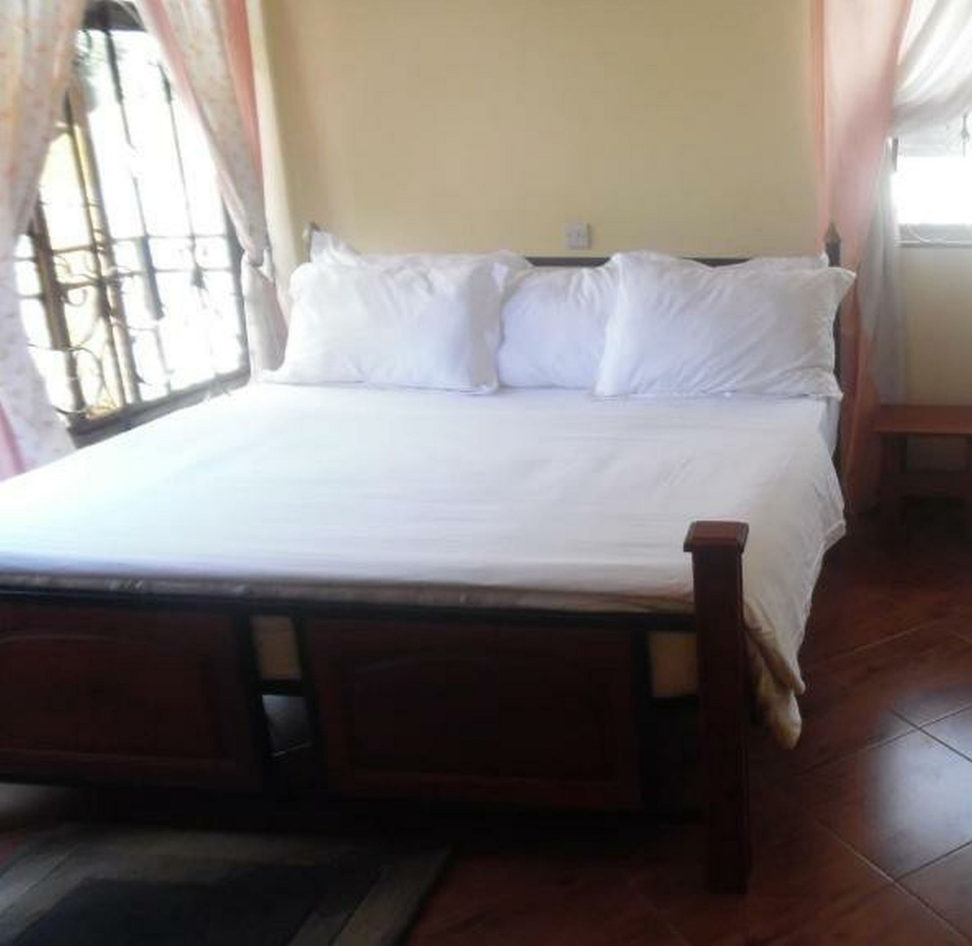 Una cama con ropa de cama blanca, un cabecero de madera y una ventana con cortinas.