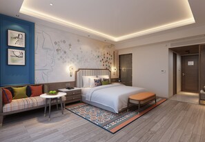 Un dormitorio moderno con una cama grande, un sofá, una mesita con fruta y una alfombra estampada.