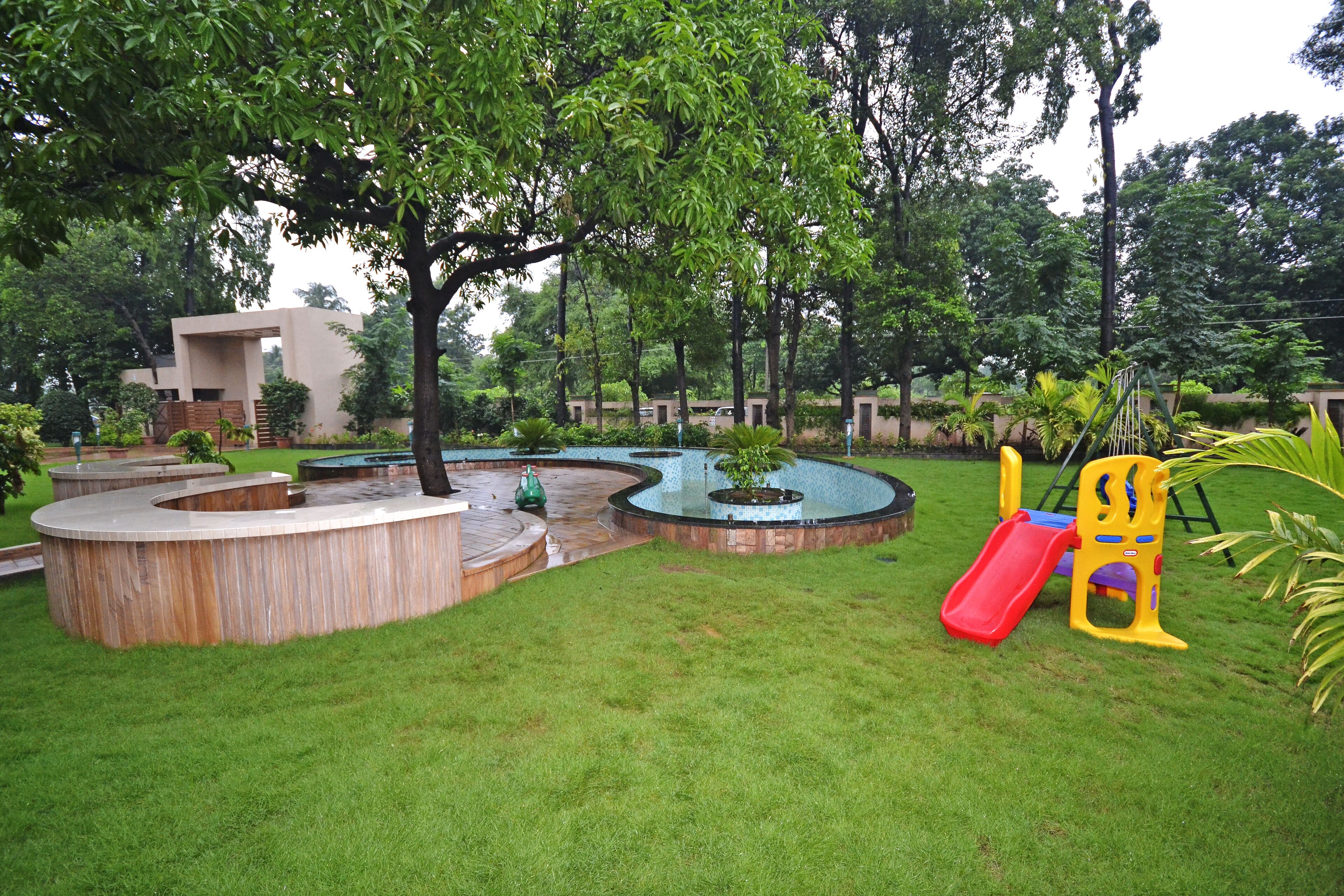 A playground with a slide and climbing structures, surrounded by grass and trees.