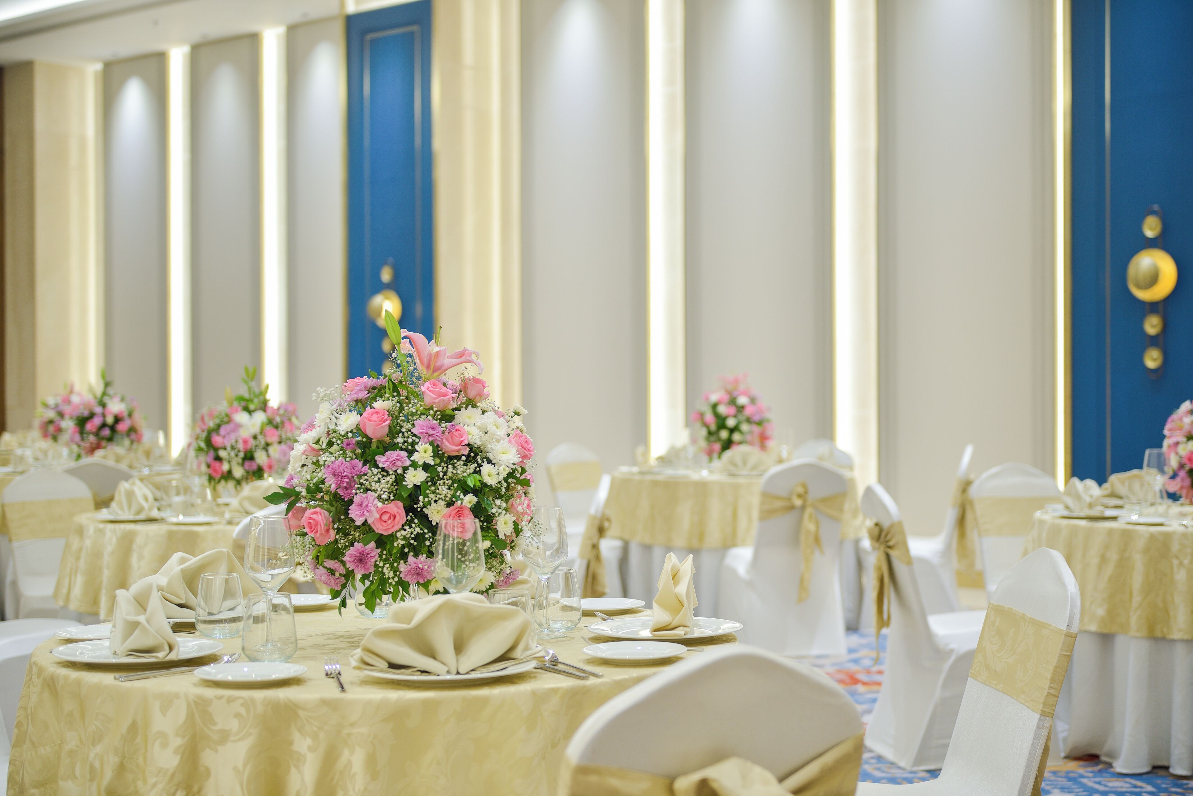 A banquet hall with round tables, white chairs, and floral centerpieces.