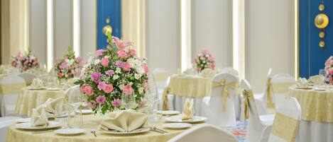 A banquet hall with round tables, white chairs, and floral centerpieces.