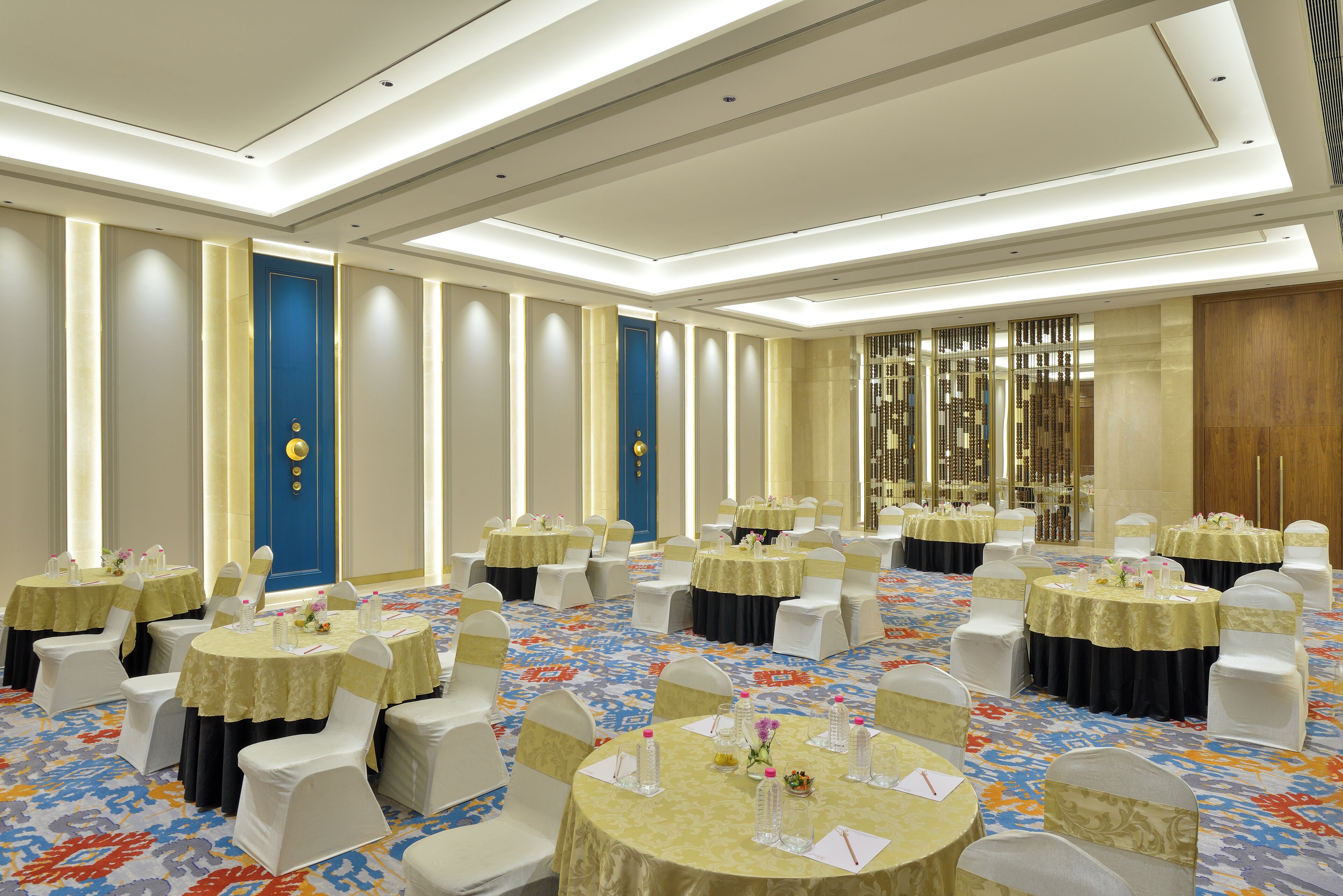 A banquet hall with round tables, white chairs, and a patterned carpet.