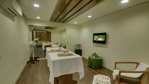A room with a wooden floor, a white table with a green tablecloth, a television on the wall, and a chair. - Boulevard9, Nadiad – IHCL SeleQtions (Nadiad)