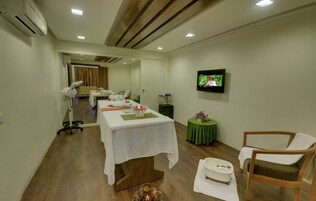 A room with a wooden floor, a white table with a green tablecloth, a television on the wall, and a chair.
