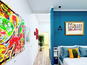 A hotel room with a bed, a wall-mounted artwork, a potted plant, and a framed picture.