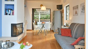 Ein modernes Wohnzimmer mit Kamin, einem Essbereich mit Glastisch und einem grauen Sofa mit roten Kissen.