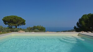 Ein klares, blaues Schwimmbecken mit Blick auf das Meer und Bäume.