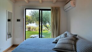 Ein Schlafzimmer mit einem großen Bett, einer Schiebetür zum Garten und einer weißen Klimaanlage an der Wand.