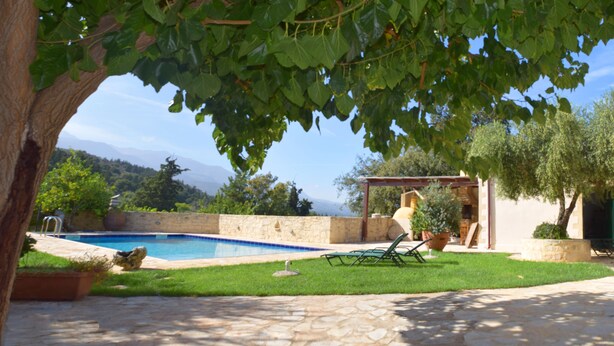 Un espace piscine agrémenté d’une terrasse en pierre, d’une pelouse et d’une pergola offrant une vue sur les montagnes.