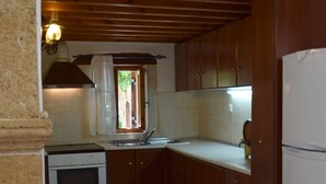 Une cuisine avec des meubles de rangement en bois, une cuisinière et un évier. Un saladier rempli de fruits est posé sur la table.