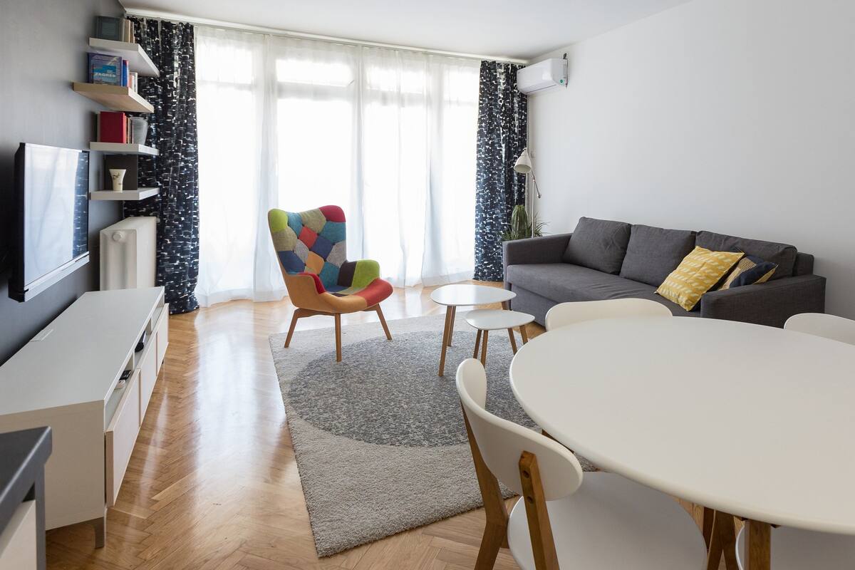 A modern living room with a sofa, a colorful armchair, a dining table, and a TV.