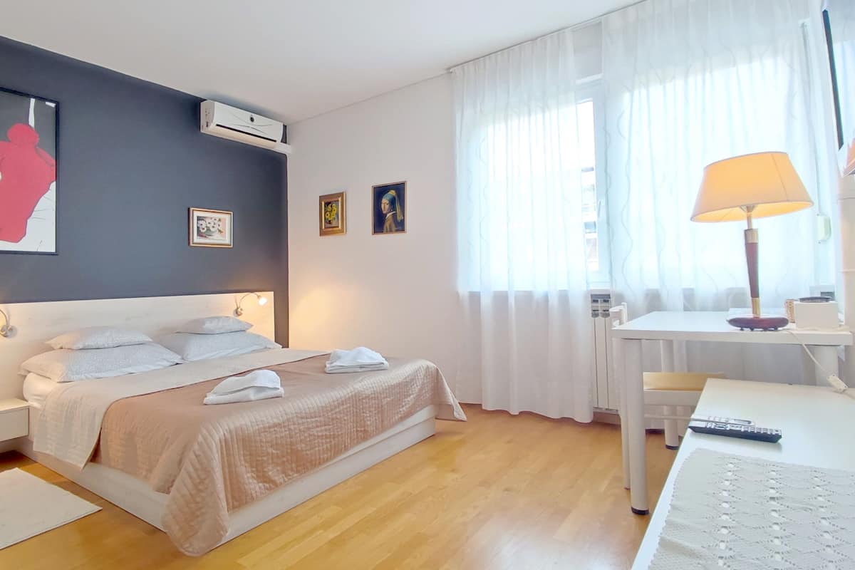 A neatly arranged bedroom with a bed, bedside tables, a desk, and a lamp.