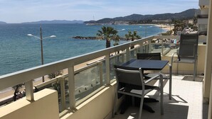 A balcony with a table and chairs, overlooking a beach and the sea. - Superb STUDIO 4 Pers / On Beach / New Condition / Sea view 180 ° except./ Parking / WIFI / AC (Le Lavandou)