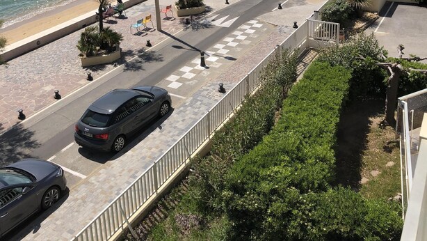 A coastal road with a beach on one side, lined with palm trees and street lamps. - Superb STUDIO 4 Pers / On Beach / New Condition / Sea view 180 ° except./ Parking / WIFI / AC (Le Lavandou)
