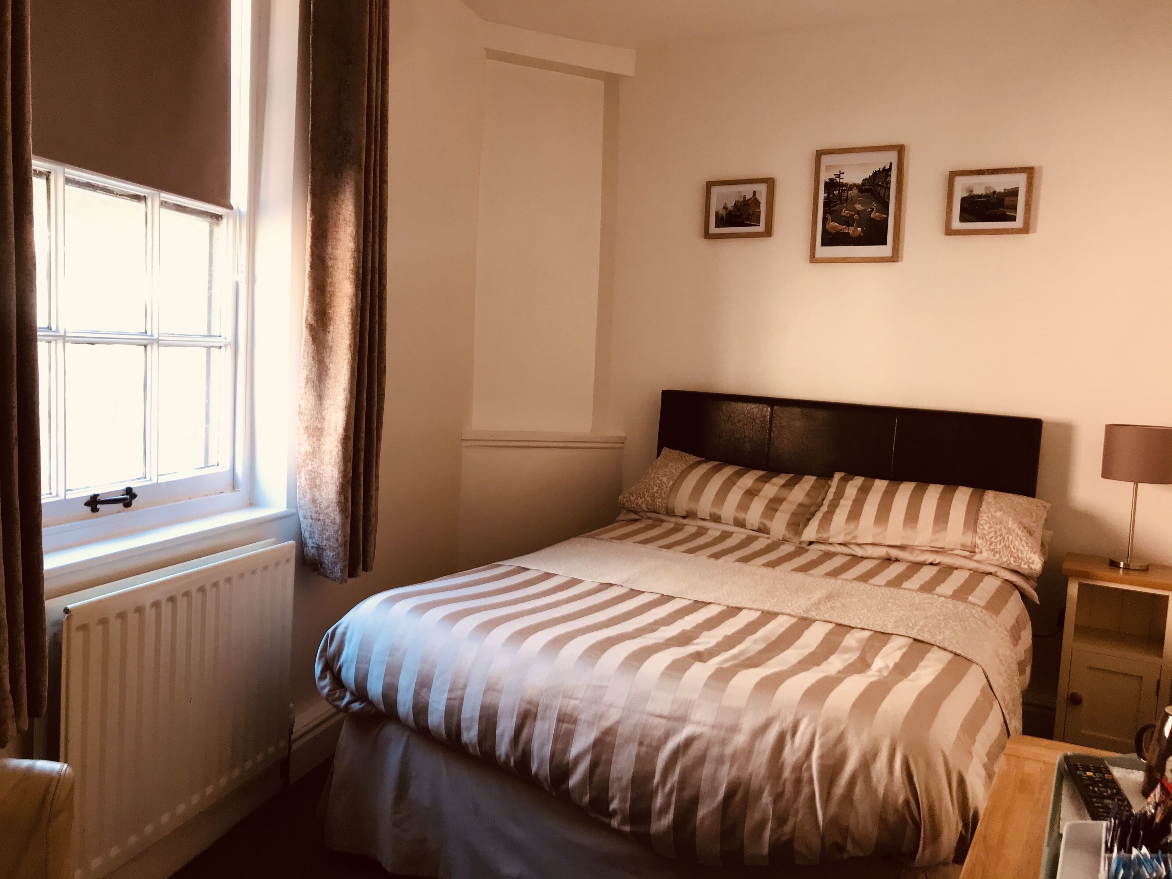 Ein Schlafzimmer mit einem Bett, einem Nachttisch, einer Lampe und drei gerahmten Bildern an der Wand.