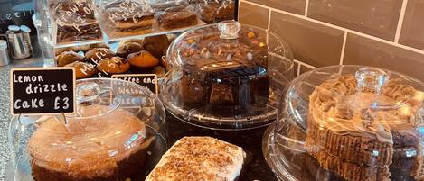 Mostrador de pastelería con diversos pasteles y dulces, incluyendo pastel de limón y pastel de chocolate, a £3.