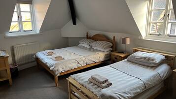 Une chambre à coucher avec deux lits en bois, un radiateur, une fenêtre et une table de chevet avec une lampe.