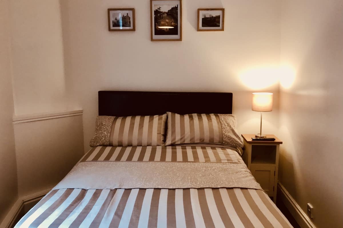 A neatly made bed with striped bedding, a dark headboard, and a bedside table with a lamp. Three framed pictures are hung on the wall above the bed.